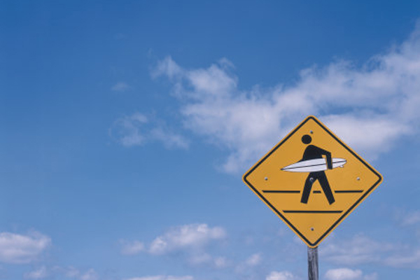 lit fuze surfer pedestrian crossing sign against blue sky created by Daniel Billotte and Matthew Flansburg in Santa Cruz California 2001 viral vandalism project to improve city signs with appropriate surf branding fLANSBURG dESIGN